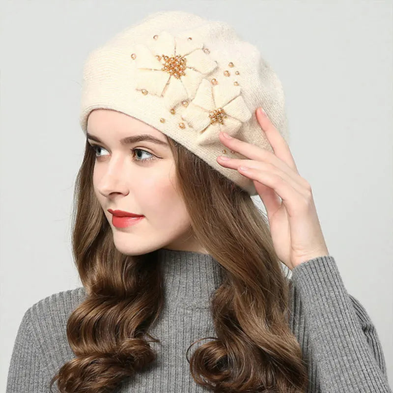 Woman wearing a beige knit hat with decorative elements on a plain background