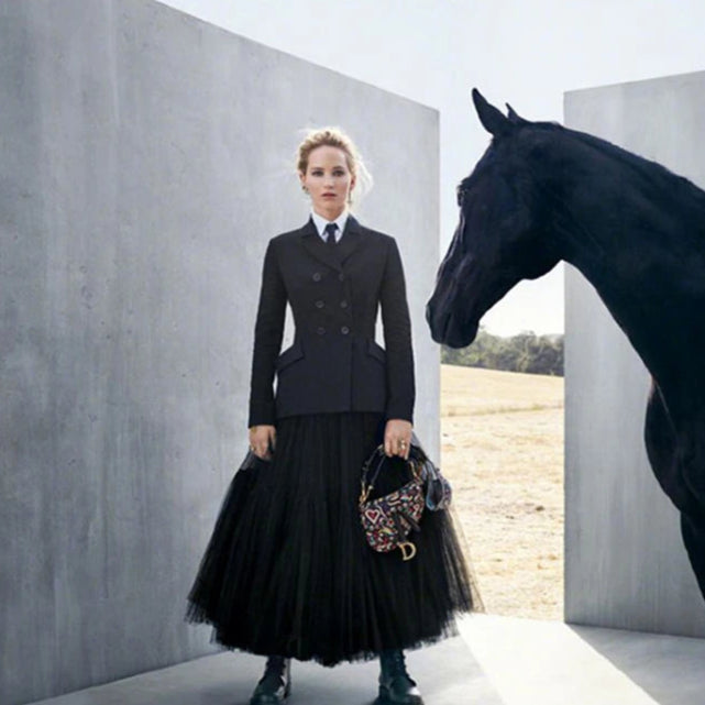 Woman in equestrian attire standing next to a horse in a minimalistic setting