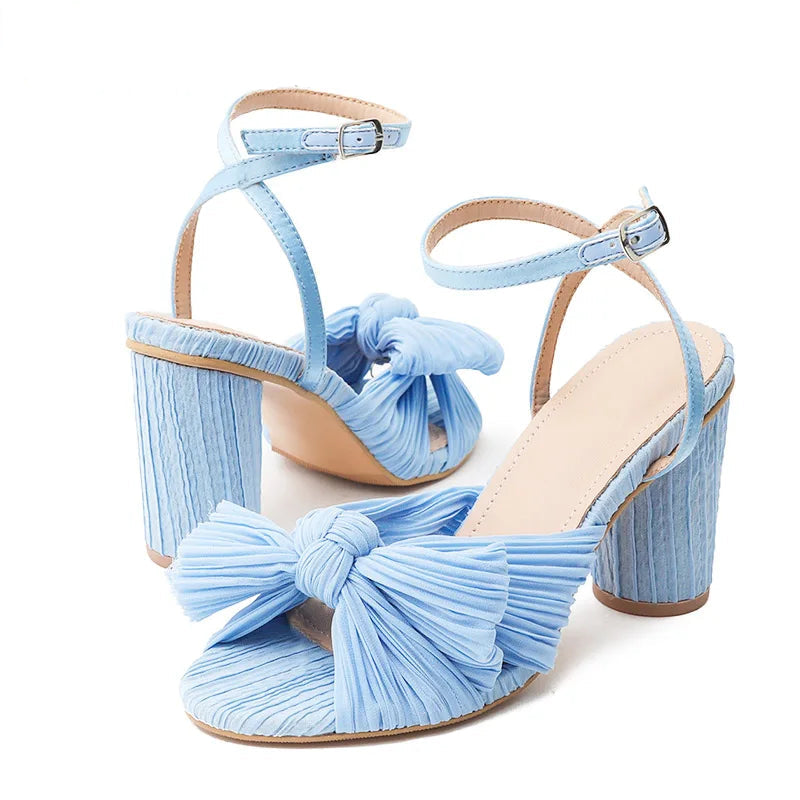 Light blue high-heeled sandals with pleated design and bow details on a white background.
