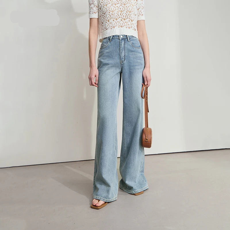 Woman wearing light blue jeans and a white lace top, holding a brown handbag on a plain background with AMII branding. - HER SHOP