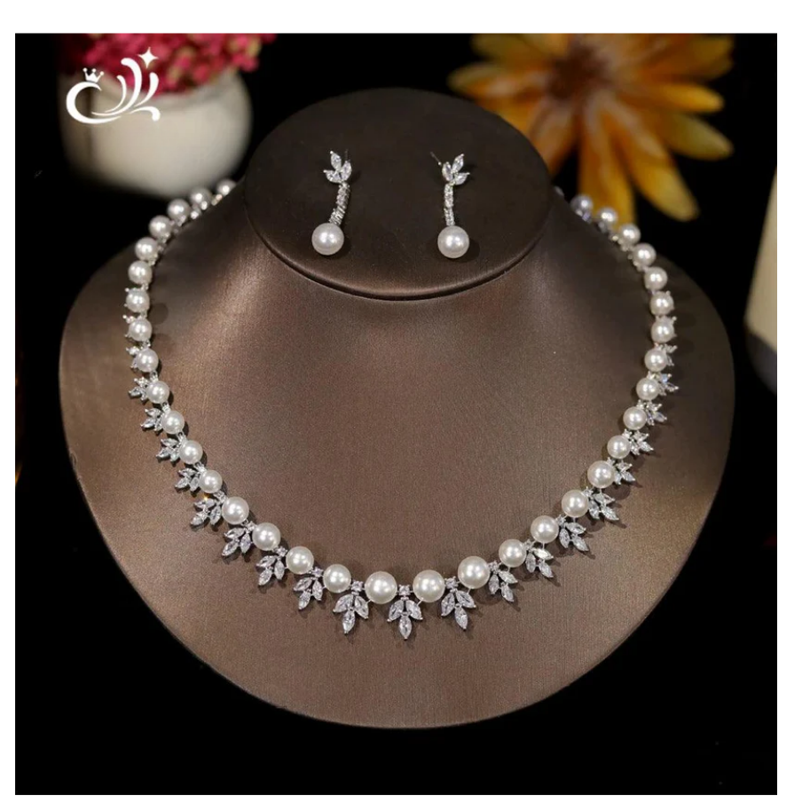 Pearl necklace and earrings set on a brown stand with flowers in the background