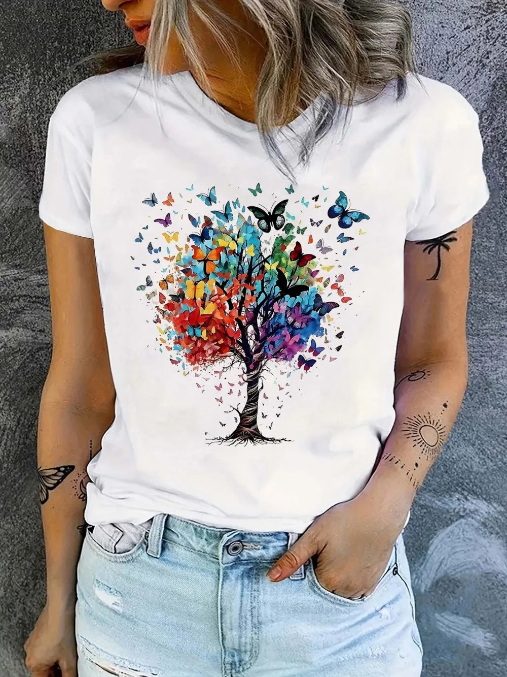 Person wearing a white t-shirt with a colorful tree and butterfly design against a gray background.