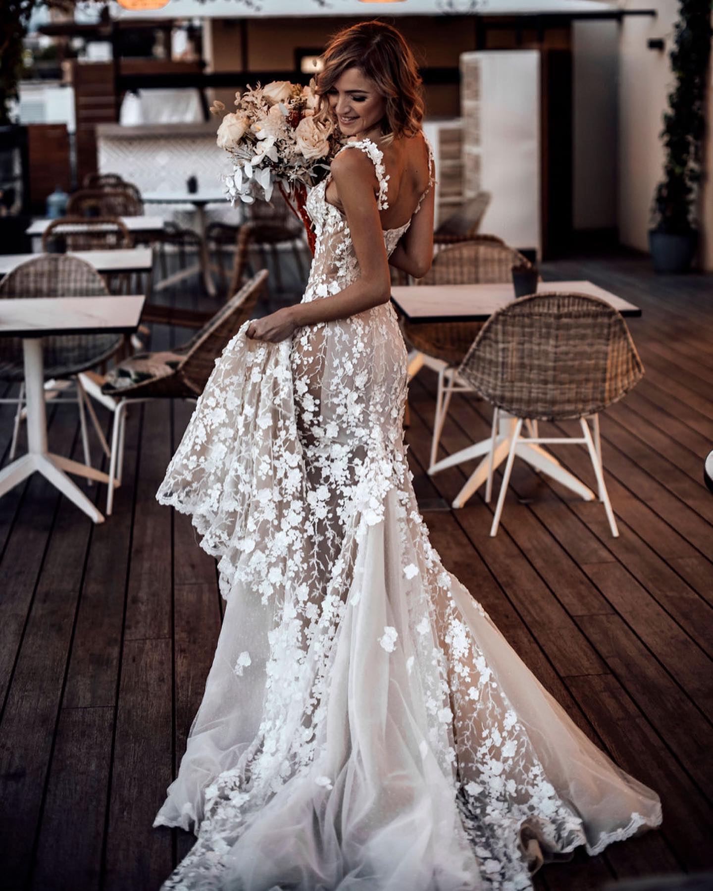 Woman in a floral dress standing in an outdoor setting with tables and chairs.