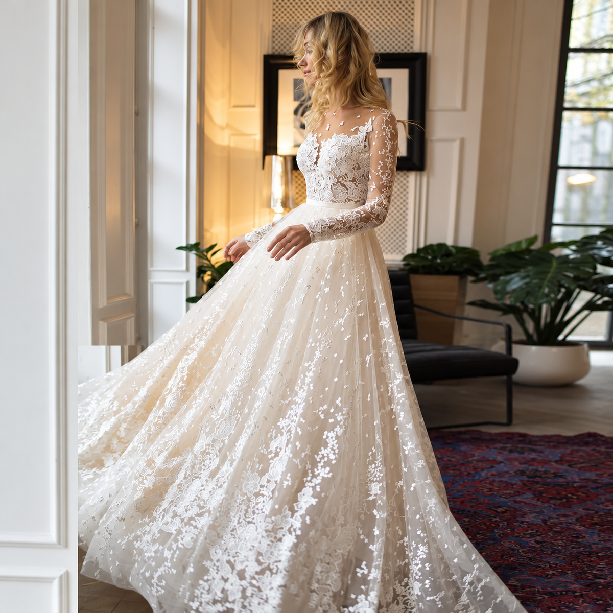 A woman wearing a voluminous ivory lace wedding gown with long sleeves and a fitted bodice, standing in a bright indoor room with plants and framed wall art. - HER SHOP®