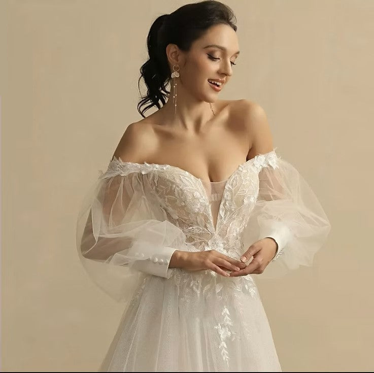 Woman wearing a white off-shoulder dress with sheer sleeves against a beige background