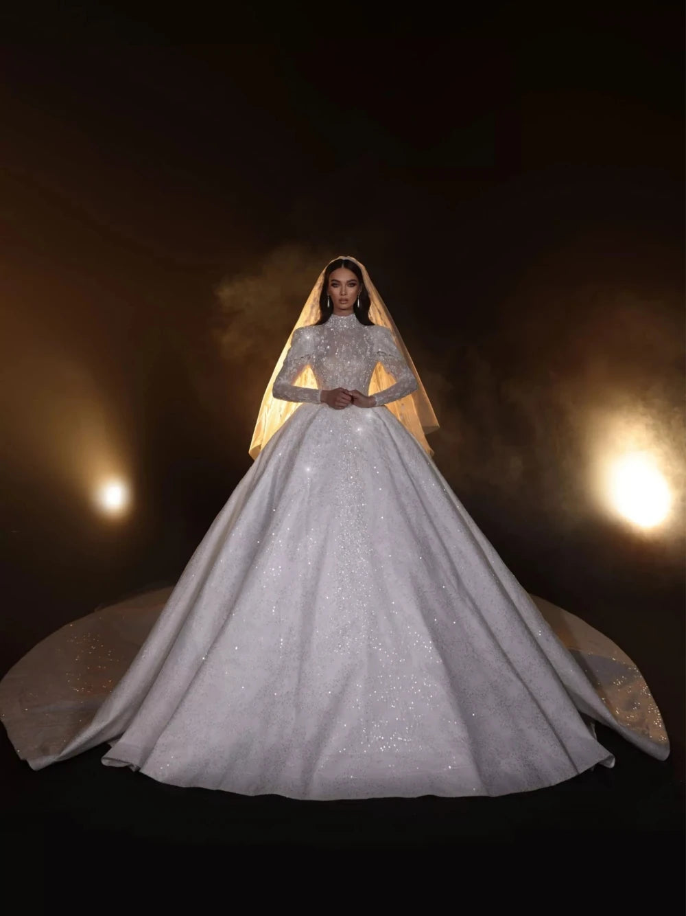 Woman in a sparkling silver wedding gown with a long train against a dark background.