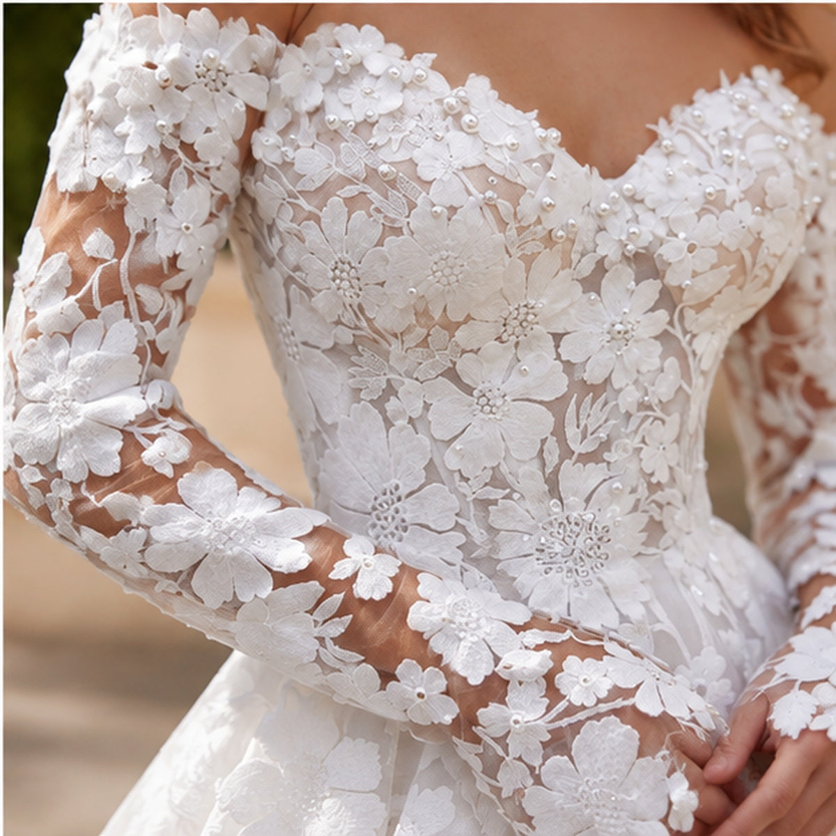 Close-up of a white floral lace wedding dress with long sheer sleeves and a sweetheart neckline, shown on a model.