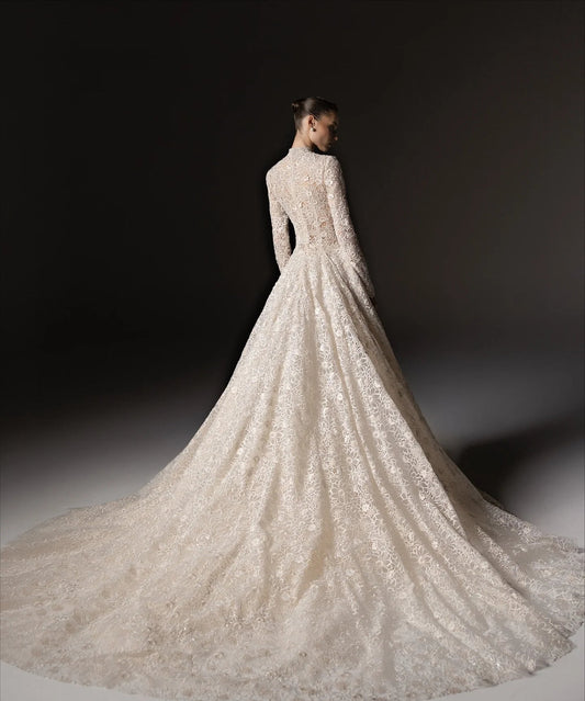 A model wears a high-neck, long-sleeved A-line modest wedding gown with intricate floral lace embroidery and a matching sheer veil. The brand name 'LISM' is visible in the top left corner against a dark studio background. - HER SHOP®