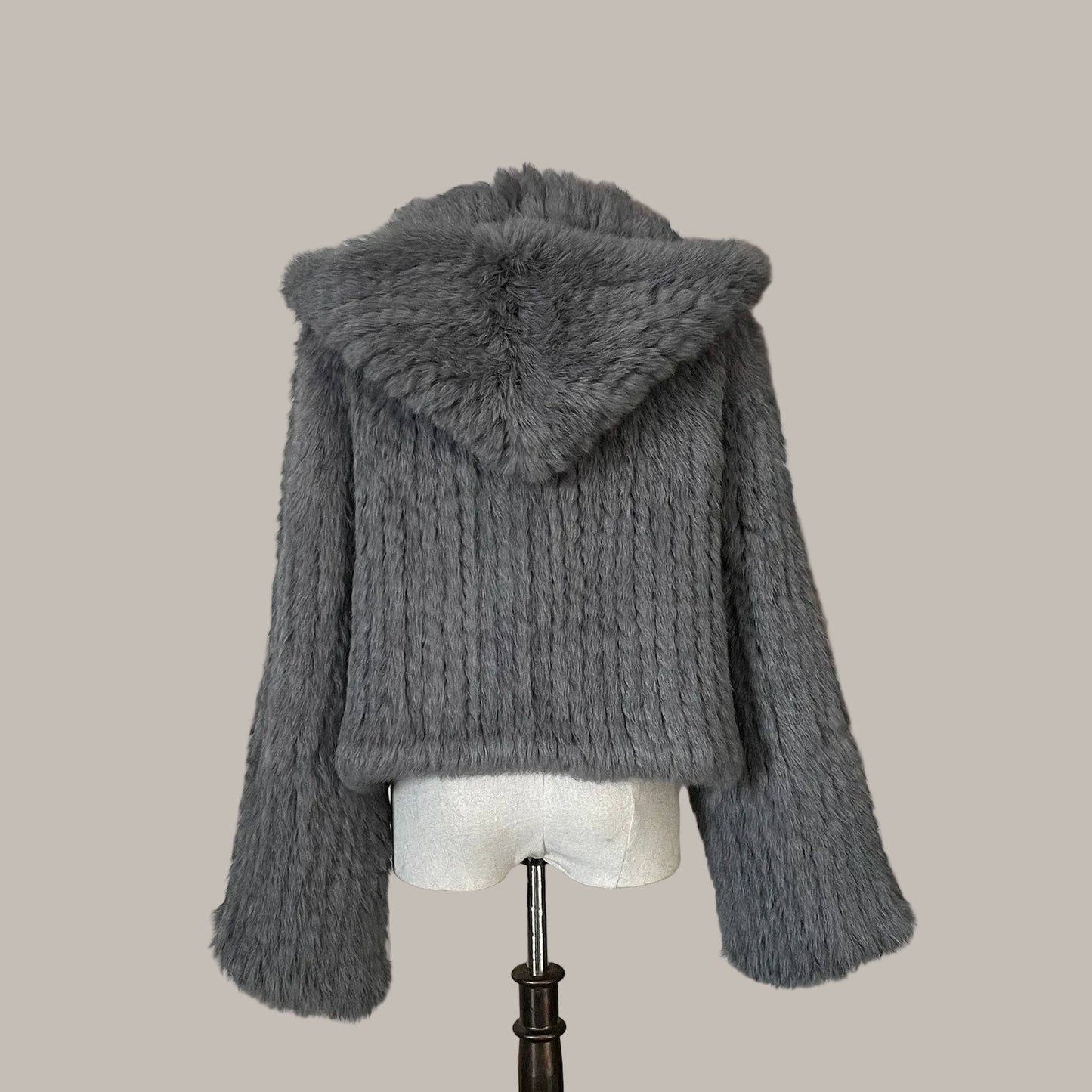 Gray knitted jacket with fur hood on a mannequin against a decorative wall.