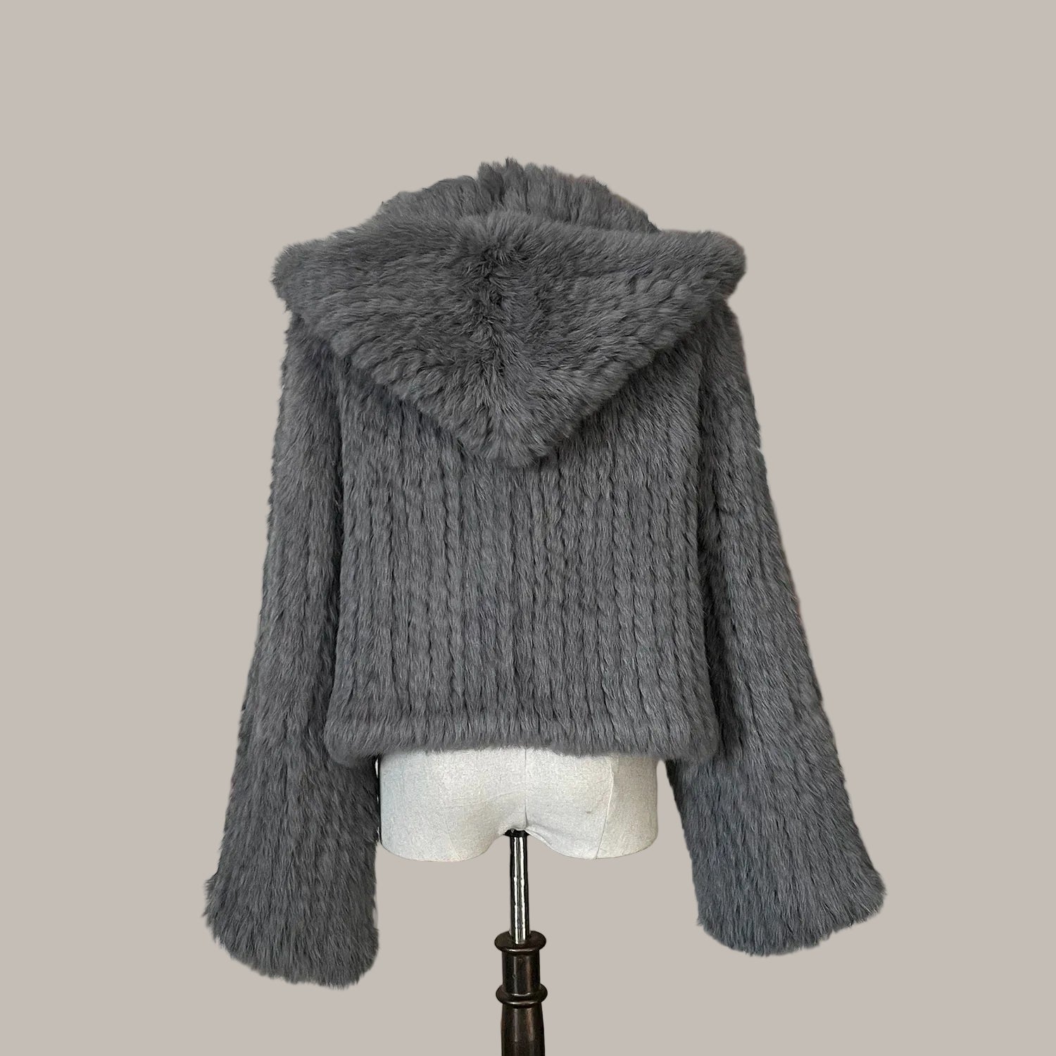 Gray knitted jacket with fur hood on a mannequin against a decorative wall.