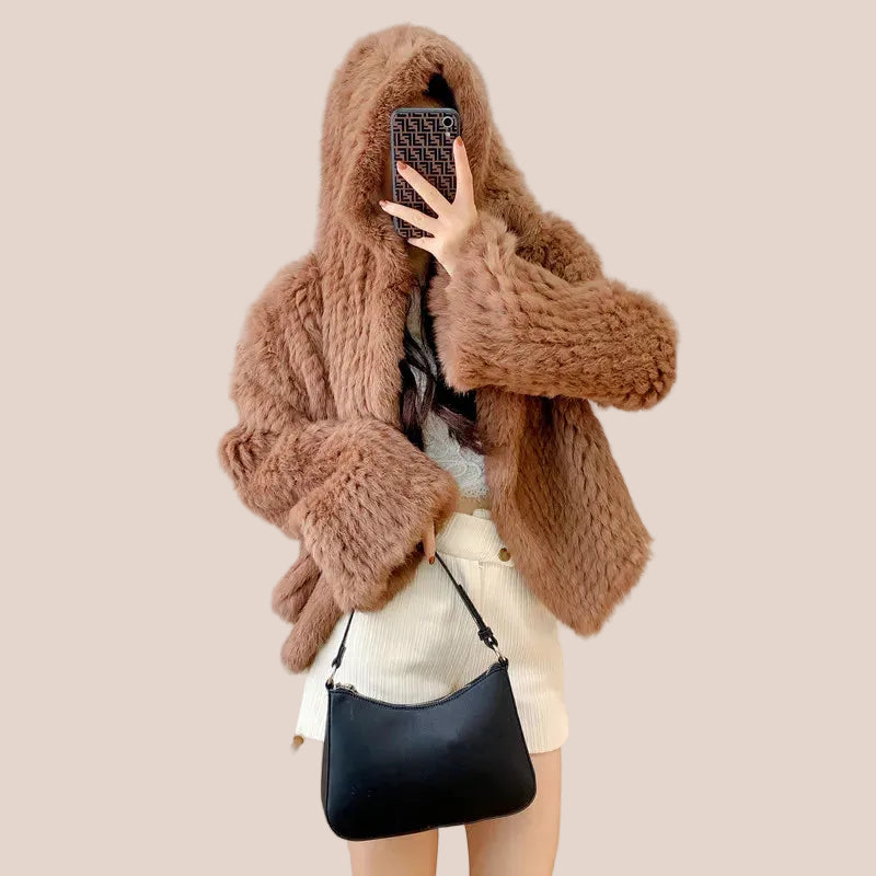 Person wearing a brown knitted hoodie in a room with a white wall and decorative elements.