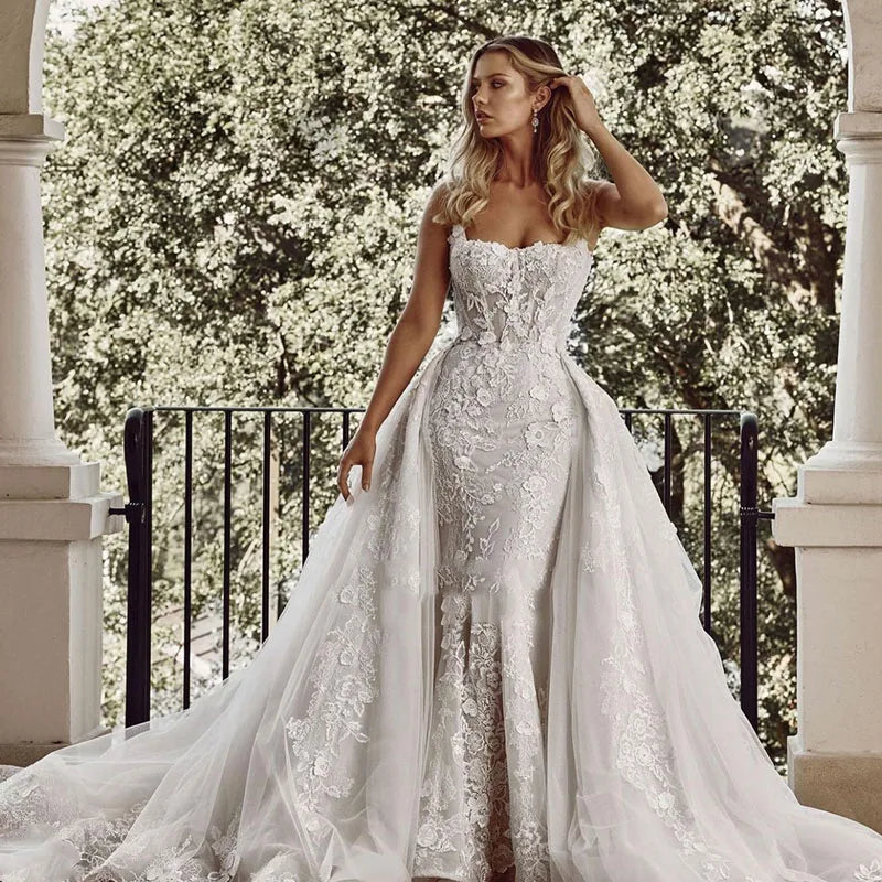 Woman in a white lace wedding dress standing outdoors with greenery in the background