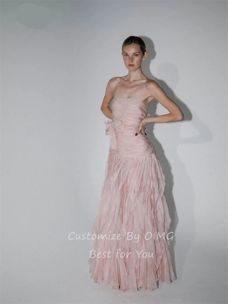 A model wearing a strapless light pink gown with a ruched bodice and a layered, ruffled tulle skirt, posed against a plain light gray studio background. The brand name 'OIMG' is visible in the top left corner, and a watermark 'Customize By OIMG Best For You' is at the bottom.