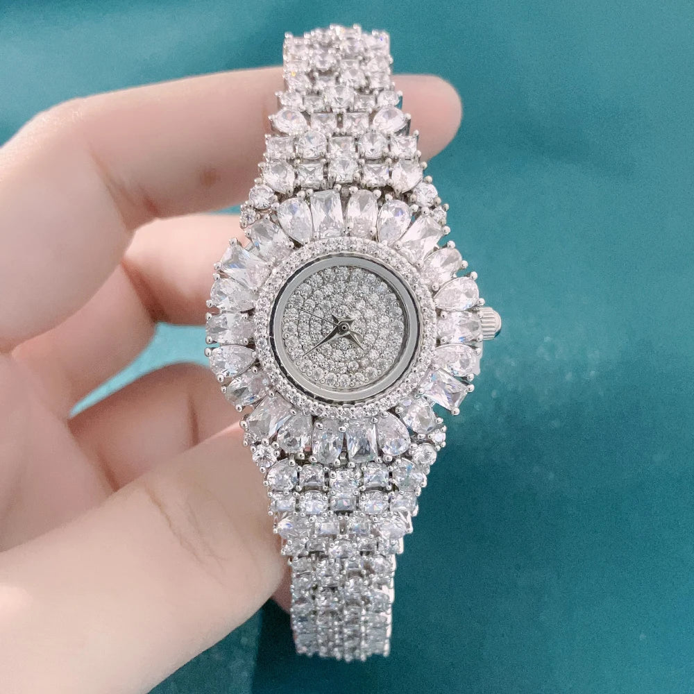 Luxury diamond-encrusted watch held by a hand against a teal background