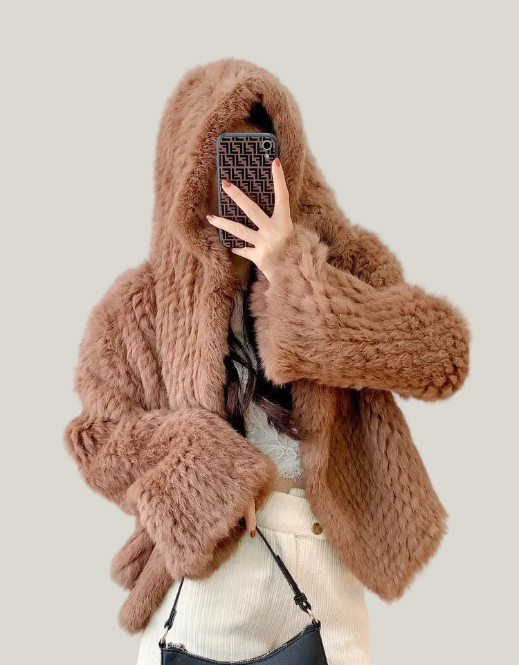 Person wearing a brown knitted sweater with a blurred face on a plain background