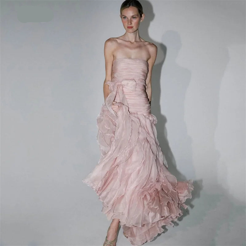 A model wearing a strapless dusty pink gown with a ruched bodice and a layered, ruffled tulle skirt, posed against a light gray studio background. - HER SHOP