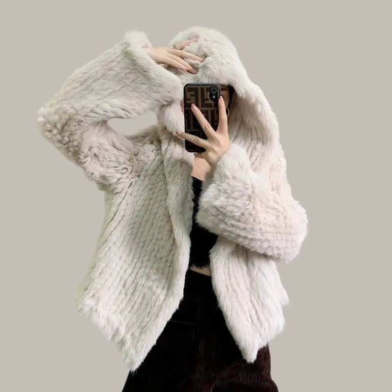 Person wearing a fluffy white coat taking a mirror selfie in a room with a painting on the wall.