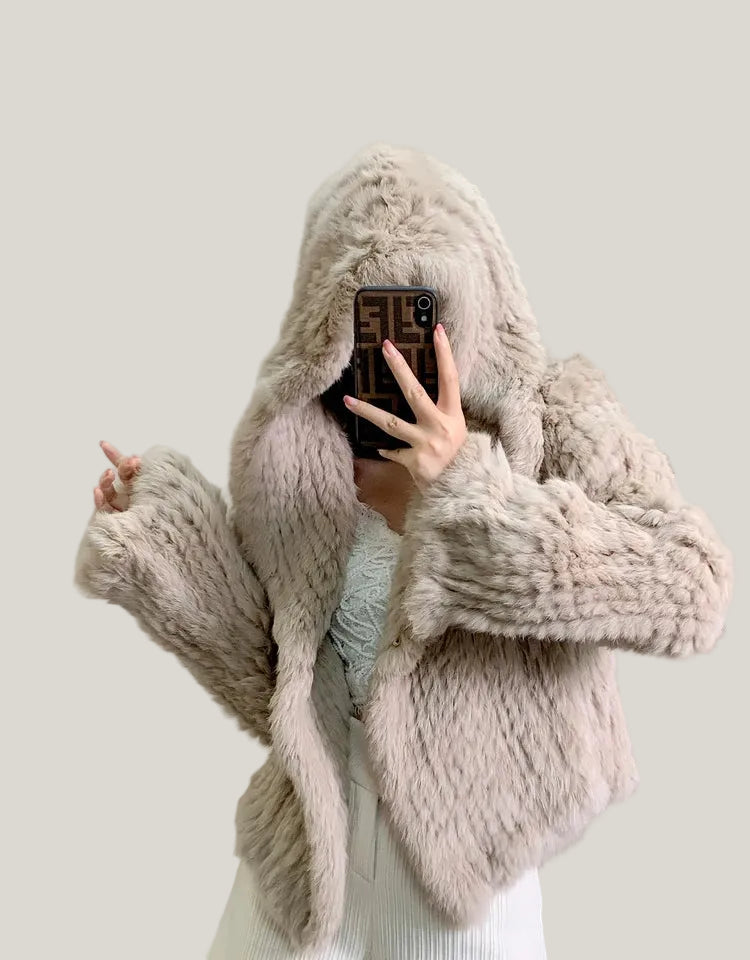Person wearing a fluffy beige hooded coat in a neutral setting