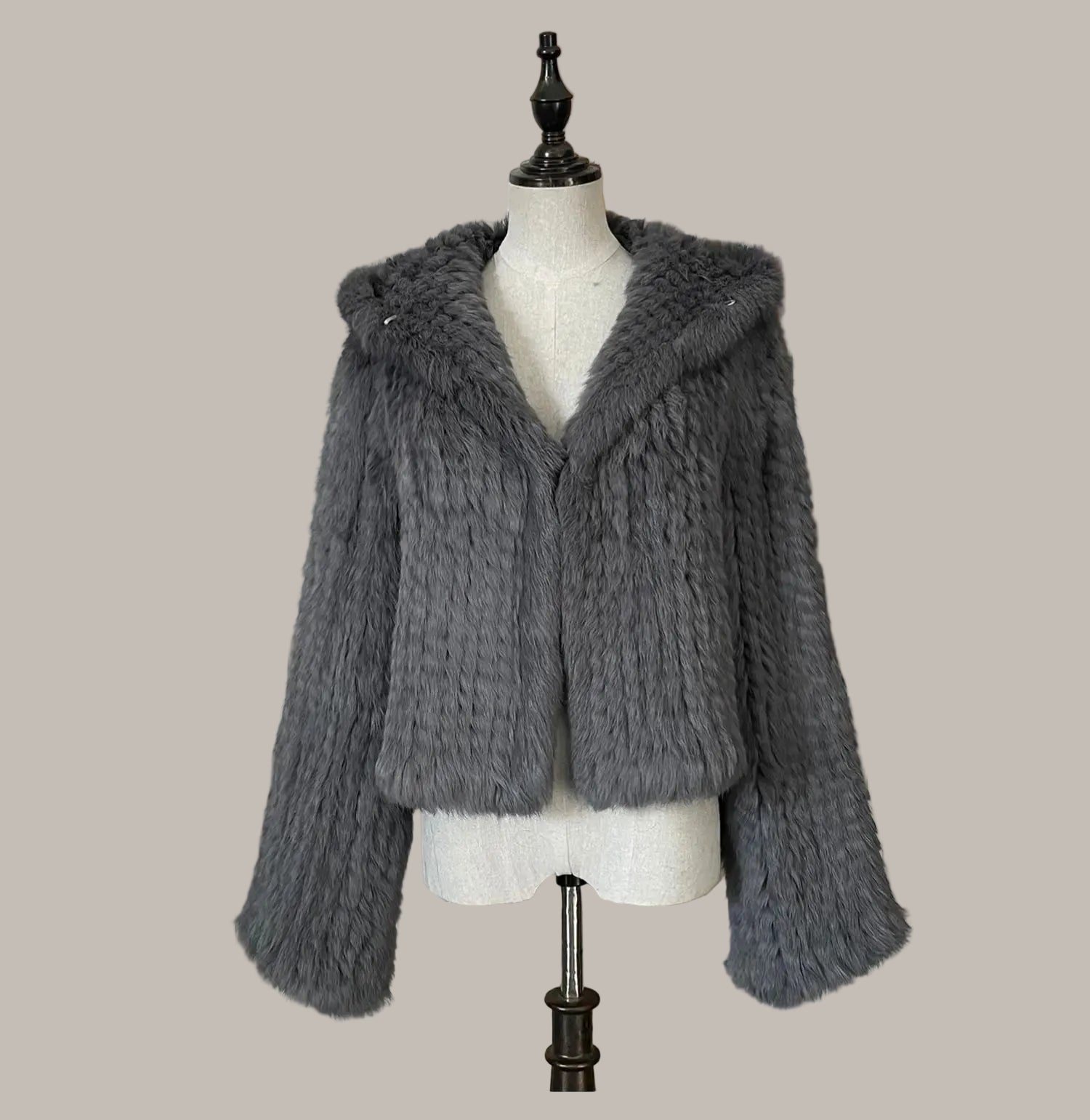 Gray knitted jacket on a mannequin against a decorative wall.