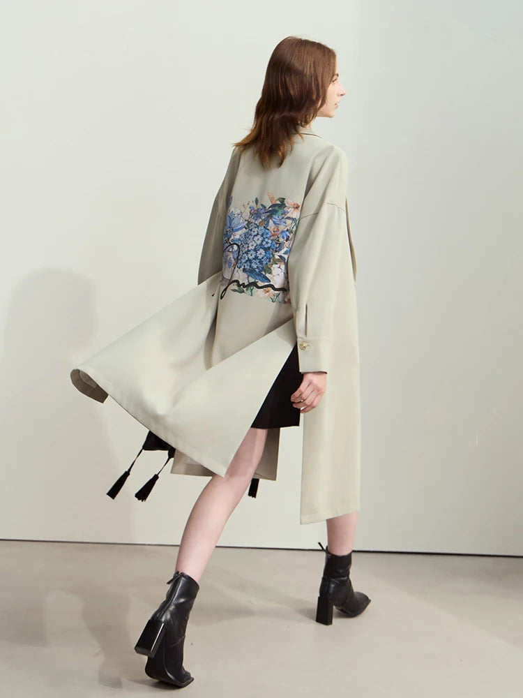 A woman modeling a beige AMII minimalist loose trench coat with a floral hydrangea print on the back, featuring a lapel collar and drop cuff design. - HER SHOP