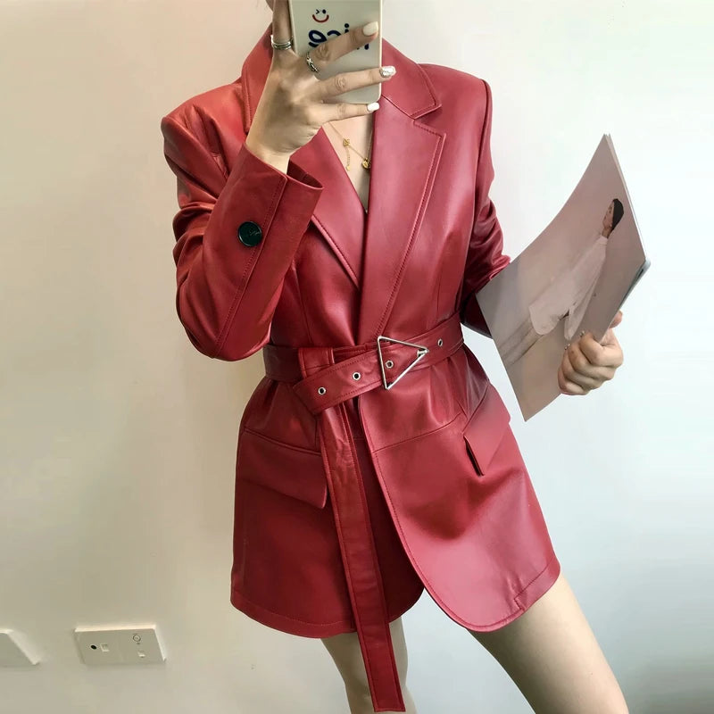 Person wearing a red leather coat with a belt, holding a phone and a magazine.