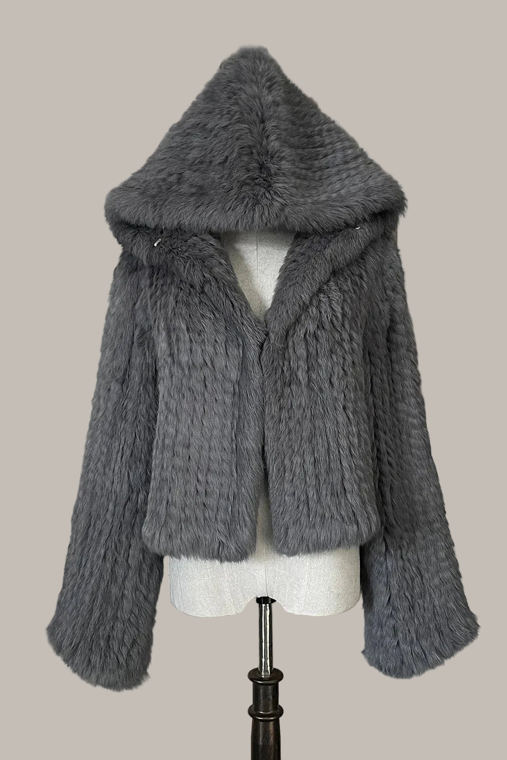 Gray knitted jacket with fur hood on a mannequin against a decorative wall.
