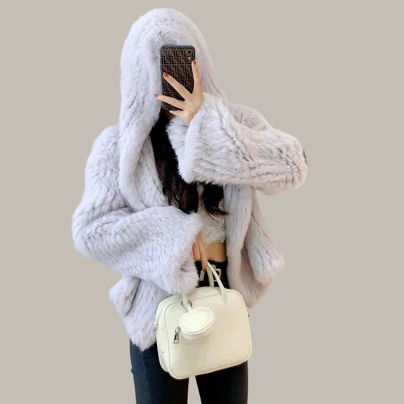 Person wearing a fluffy white coat taking a mirror selfie indoors.