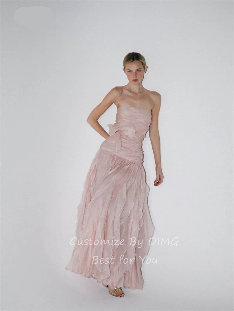 A woman modeling a strapless dusty pink gown with a gathered waist and a flowing ruffled skirt, photographed against a plain light gray studio background. The brand name OIMG appears in the top left, and watermark text at the bottom reads 'Customize By OIMG Best for You'.