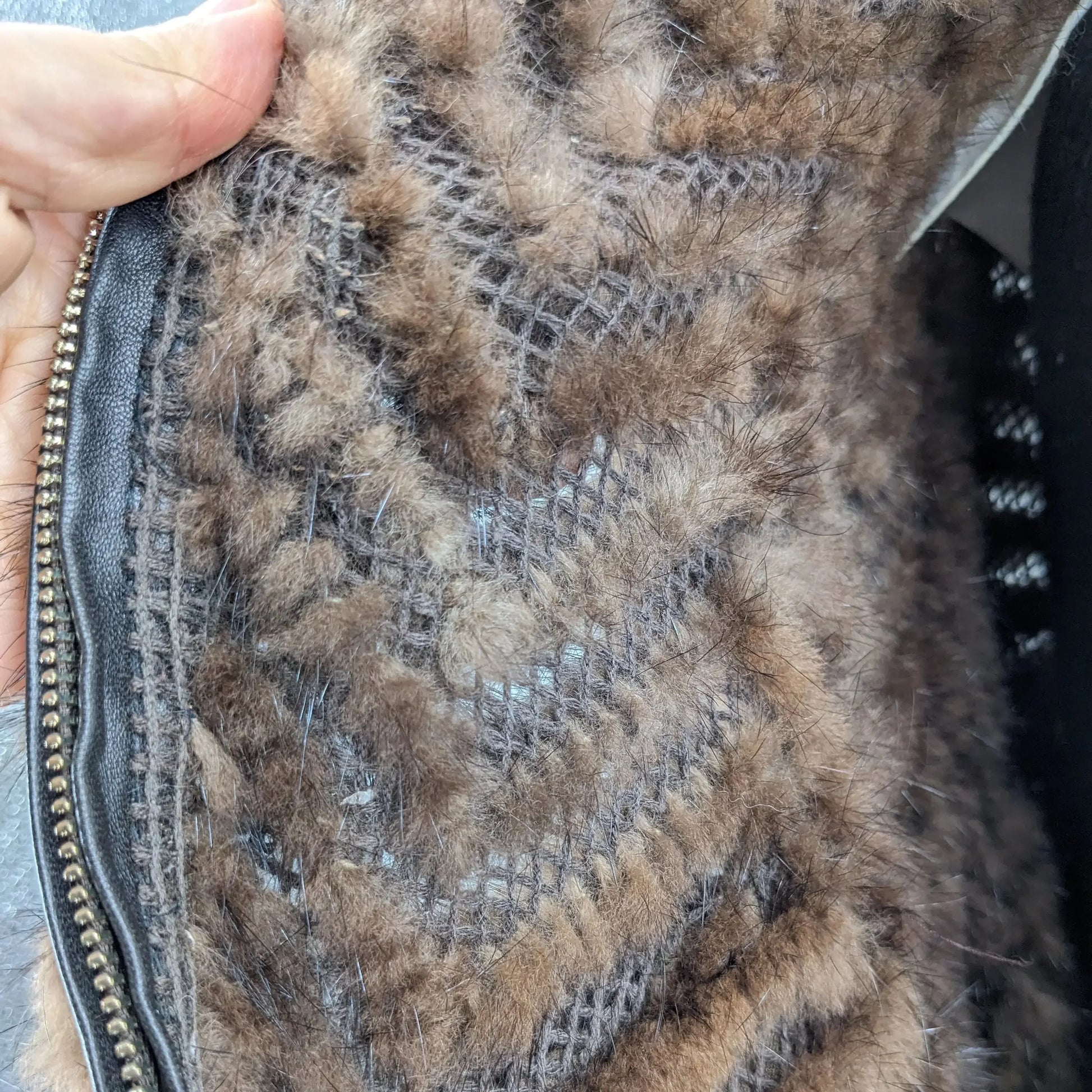 Close-up of a textured brown fabric with a zipper, held by a hand.