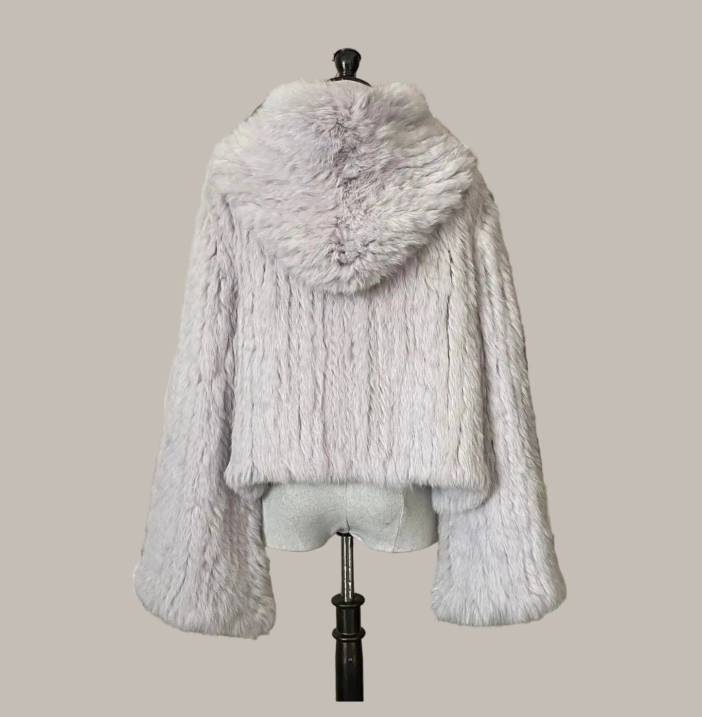 Gray fur coat on a mannequin against a decorative wall with flowers and patterns.