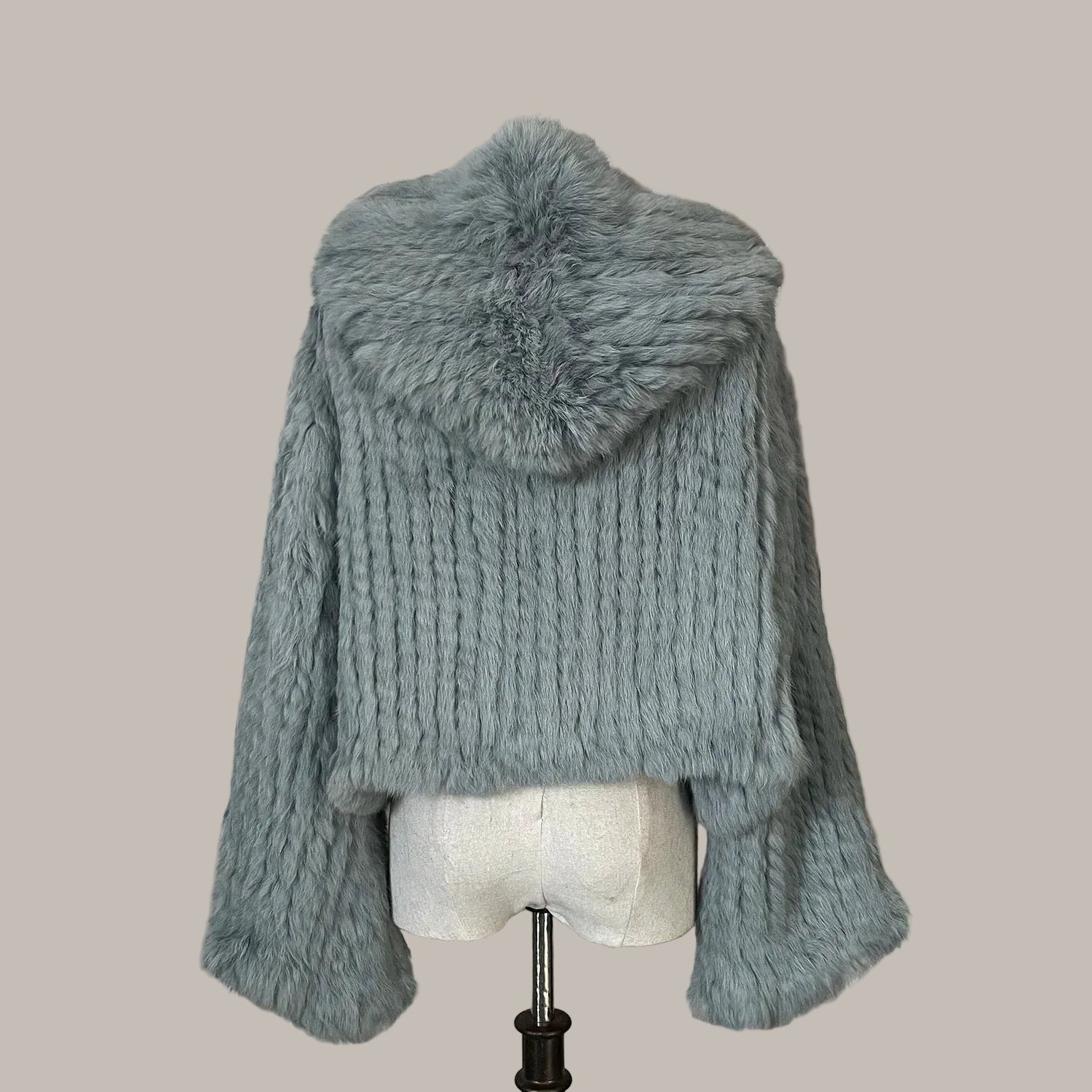 Gray knitted poncho with fur trim on a mannequin against a decorative wall.