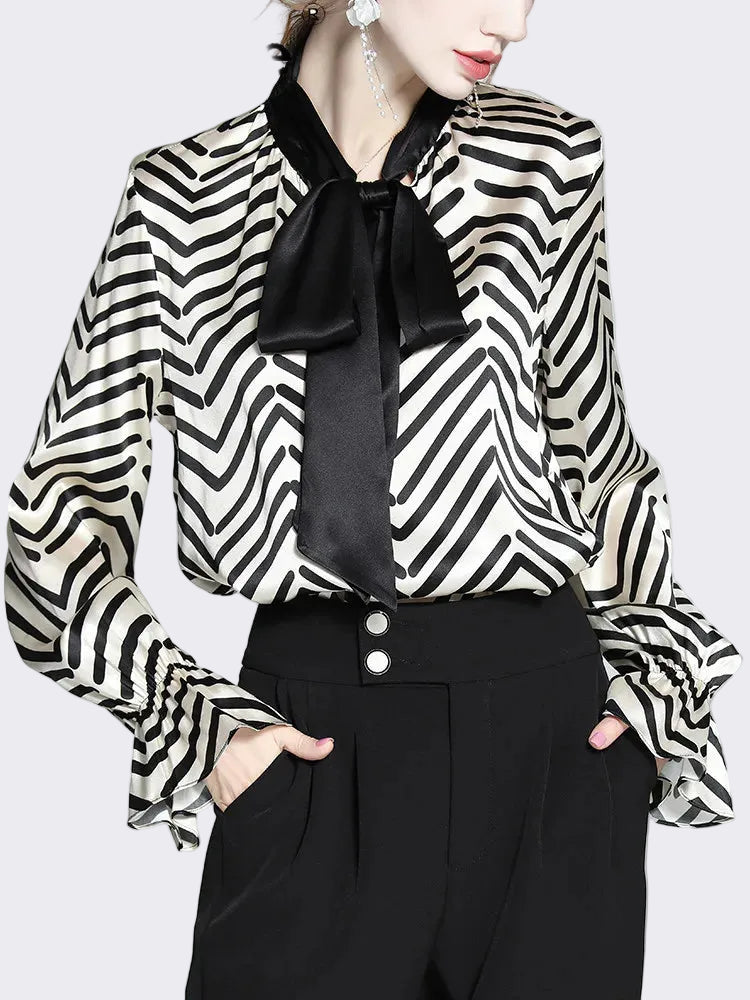 Person wearing a black and white striped blouse with a black bow tie on a light gray background.