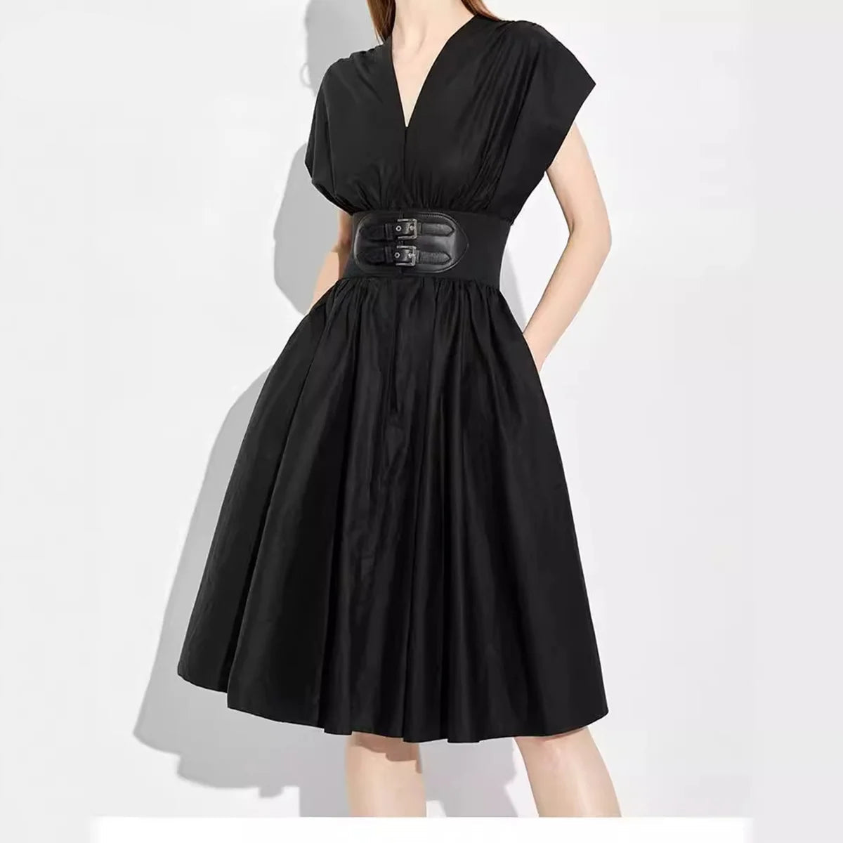 A woman wearing a black V-neck midi dress with cap sleeves, a gathered waist, and a wide black belt with double silver-tone buckle details. The image is set against a plain white background with a soft shadow, and the brand name 'CHCH' is visible in the top-left corner.