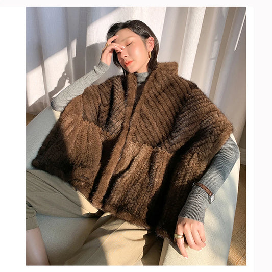 Person wearing a brown knitted poncho sitting on a chair with light curtains in the background - HER SHOP