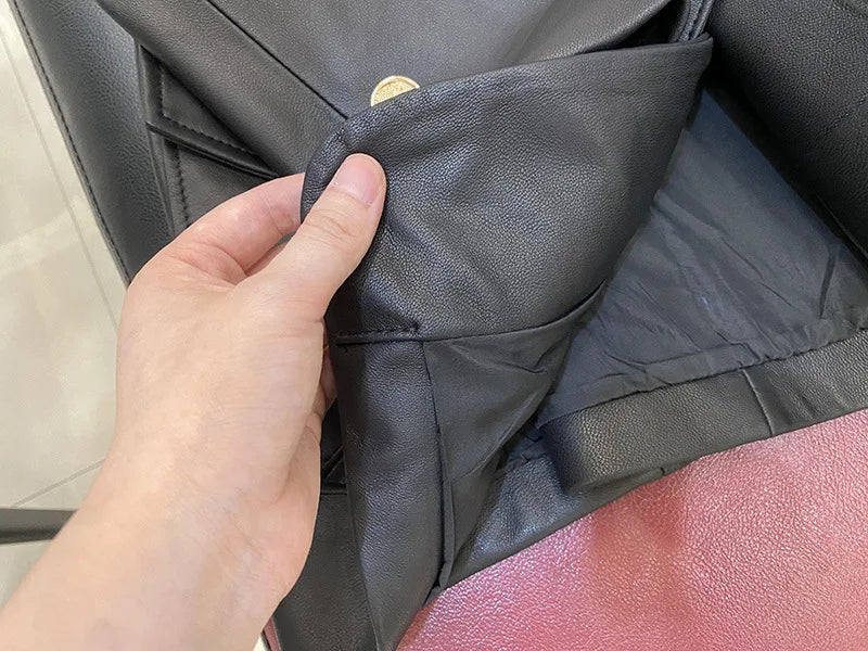 Close-up of a hand holding a black leather bag with a gold logo.