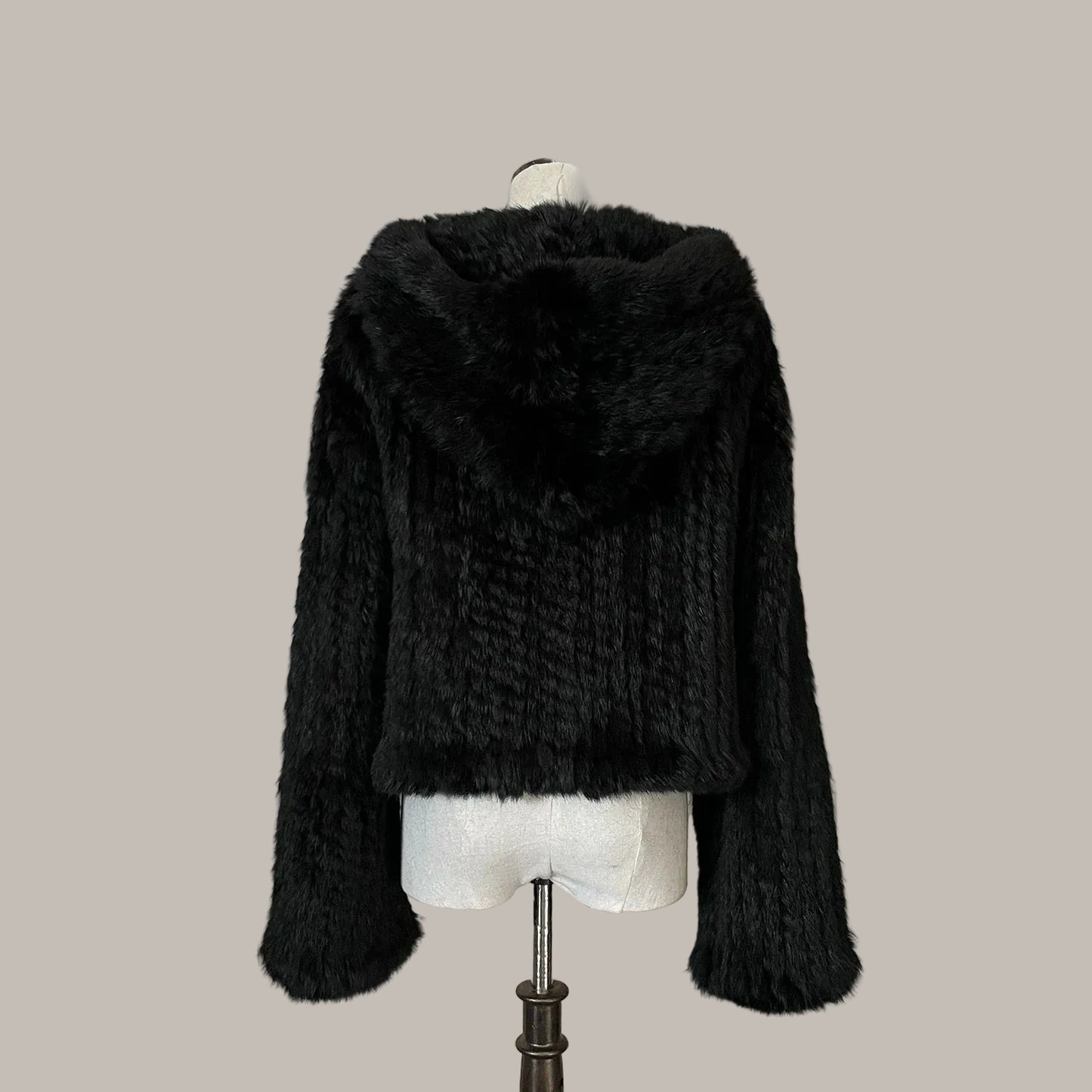 Black fur jacket on a mannequin against a decorative wall with floral elements.