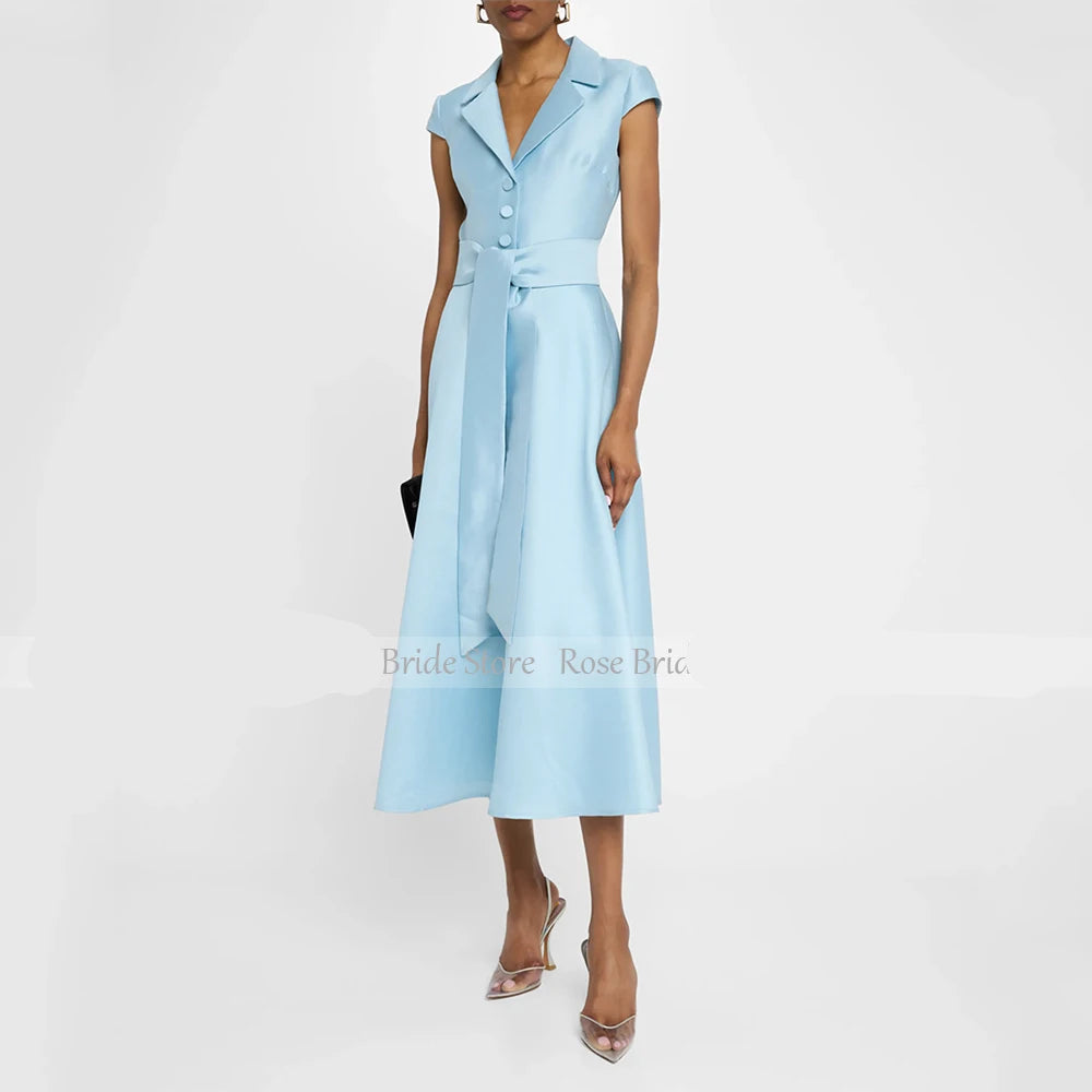 A woman models a light blue midi dress with a structured collar, cap sleeves, a button-front bodice, and a matching waist tie, photographed against a plain light background.