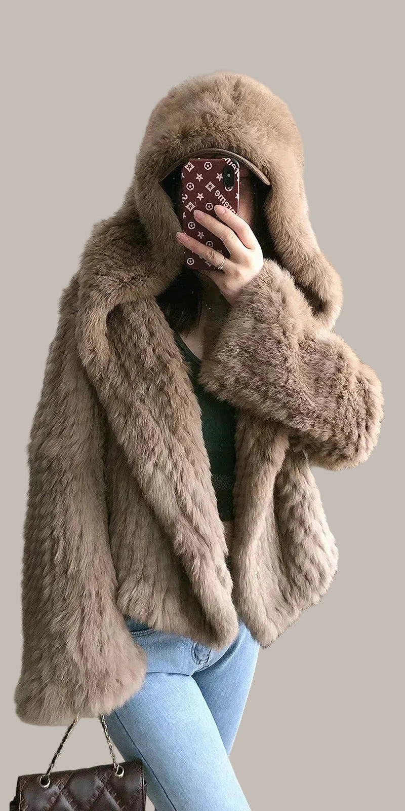 Person wearing a fur coat with a blurred face, standing against a white wall.