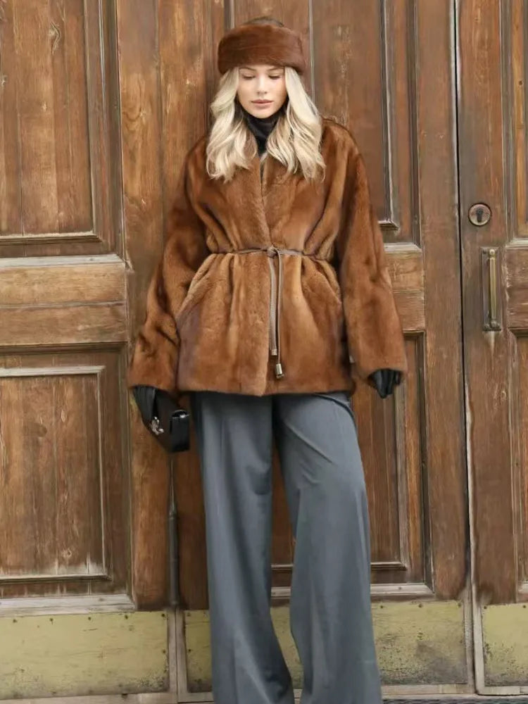 Person wearing a brown fur coat and hat standing in front of wooden doors.