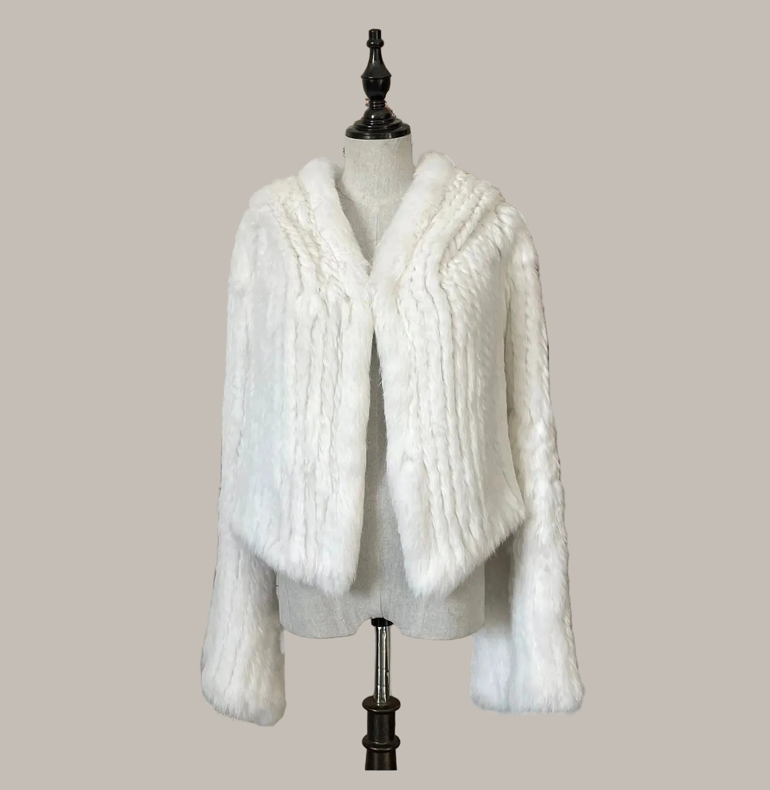 White knitted cardigan on a mannequin against a decorative wall with flowers.